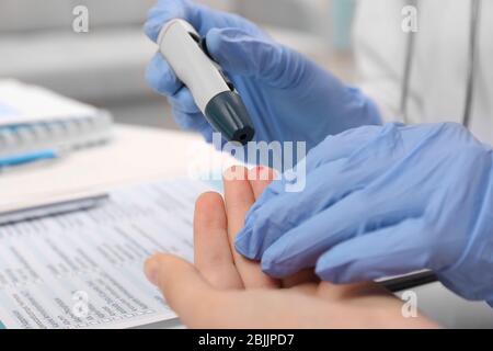 Un technicien médical en gants en latex prenant un échantillon sanguin de patient avec un stylo lancet à l'hôpital Banque D'Images