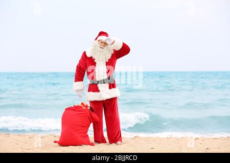 Authentique Père Noël avec grand sac rouge plein de cadeaux sur la plage Banque D'Images