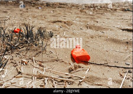 Déchets en plastique rouge sur la rive sablonneuse de la mer. Le problème de la catastrophe écologique et des déchets non recyclables Banque D'Images