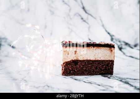 Gâteau au dessert « lait d'oiseau ». Un morceau de gâteau au chocolat dans les guirlandes et les ampoules sur une surface en marbre blanc Banque D'Images