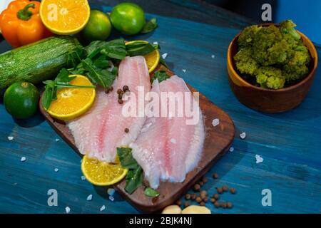 Filet de poisson avec orange, sel de grain, poivre et épinards, sur une base en bois bleu, prêt à cuire. Banque D'Images