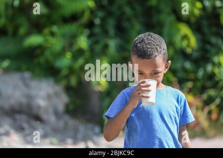 Mignon garçon africain américain boire de l'eau de la tasse en plastique, à l'extérieur Banque D'Images