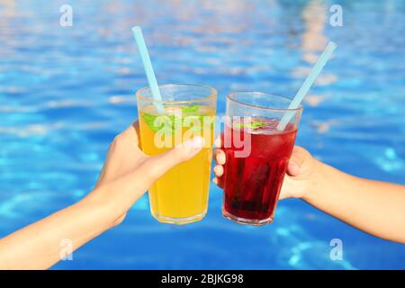 Les mains de jeunes femmes sont dotées de lunettes à clinking avec cocktails près de la piscine Banque D'Images