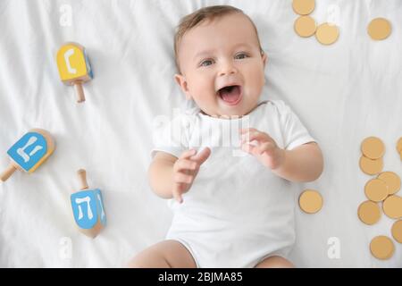 Mignon bébé drôle allongé près des dreidels et des pièces de chocolat sur le lit Banque D'Images