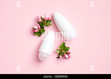 Bouteilles et fleurs désodorisantes vierges sur fond rose. Plat, vue du dessus. Mockups d'emballage antisudorifiques, soins de la peau sous les bras, protection contre la transpiration con Banque D'Images