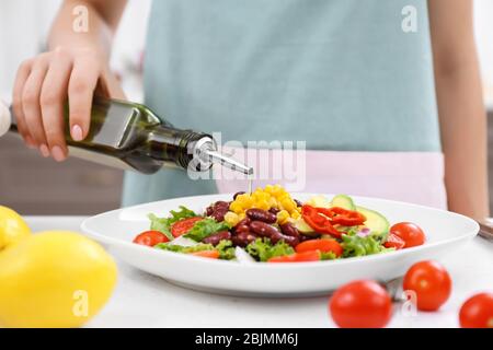 Femme versant de l'huile d'olive sur une salade de légumes dans la cuisine Banque D'Images
