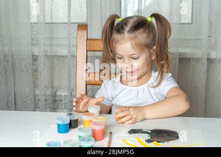fille 3-4 ans joue avec des boîtes de peintures. créativité des enfants pendant la période de l'auto-isolation et de la quarantaine en rapport avec le coronavi Banque D'Images