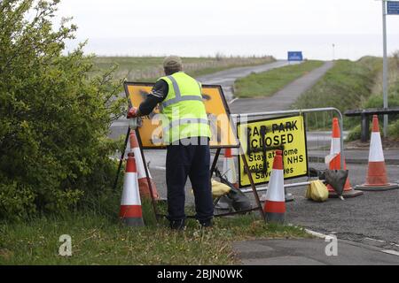 Un travailleur retire un spray à la hâte peint sur un panneau à l'entrée d'une route fermée et d'un parking près du phare de Whitley Bay, Northumberland. Graffiti a été affiché sur des panneaux dans plusieurs parkings le long de la route côtière de Northumberland alors que le Royaume-Uni continue à se verrouiller pour aider à freiner la propagation du coronavirus. Banque D'Images