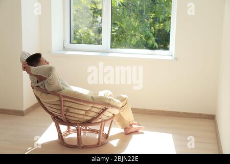 Jeune homme reposant dans un fauteuil près de la fenêtre à la maison Banque D'Images