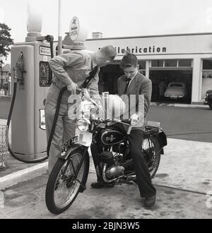 Dans les années 1950, un jeune homme assis sur un British a fait de l'Excelsior une moto extérieure dans un garage où l'essence était mise dans son réservoir par un préposé à la piste en uniforme, Angleterre, Royaume-Uni. Basé à Coventry, l'Excelsior était le premier fabricant britannique de motocyclettes, ayant fait son propre 'motor-vélo' en 1896. Banque D'Images