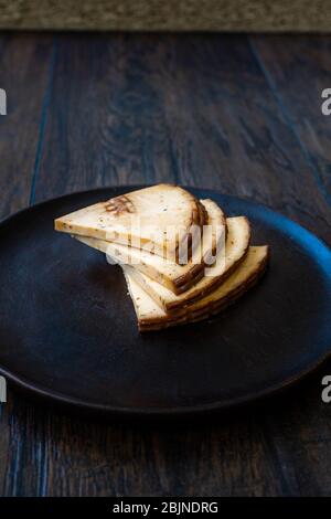 Tranches de fromage fumé Triangle Circassian épicé sur une plaque en bois sombre aux épices. Prêt à manger. Banque D'Images