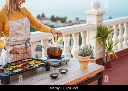 Jeune femme grill les légumes tout en préparant le dîner dans la terrasse extérieure - nourriture, style de vie sain et concept végétarien - se concentrer sur la bouteille d'huile Banque D'Images