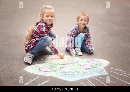 Les petits enfants qui dessinent un vaisseau spatial extraterrestre avec de la craie sur de l'asphalte Banque D'Images