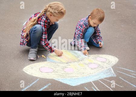 Les petits enfants qui dessinent un vaisseau spatial extraterrestre avec de la craie sur de l'asphalte Banque D'Images