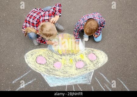 Les petits enfants qui dessinent un vaisseau spatial extraterrestre avec de la craie sur de l'asphalte Banque D'Images