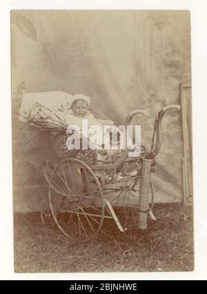 Début des années 1900, portrait maritime édouardien de bébé dans un pram élaboré, avec chien pug, toile de fond, vers 1905, Eastbourne, Sussex, Angleterre Royaume-Uni Banque D'Images