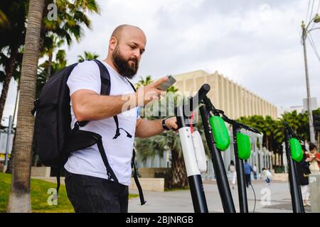 Jeune homme scannant le code qr avec son téléphone pour la location de scooter électrique. Banque D'Images