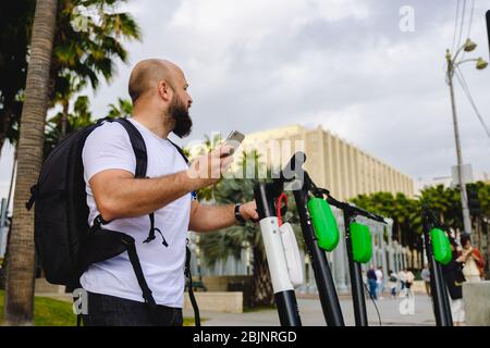 Jeune homme scannant le code qr avec son téléphone pour la location de scooter électrique. Banque D'Images