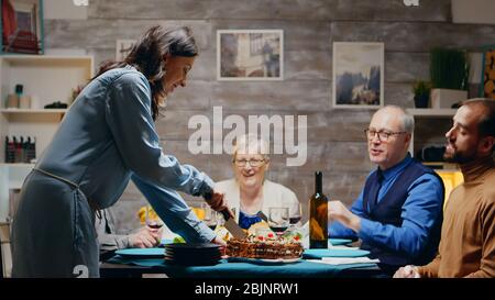 Femme caucasienne qui tranche le gâteau pour son anniversaire au dîner en famille. Banque D'Images