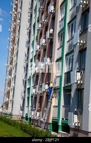 Un homme lave des fenêtres sur la rue debout sur les escaliers. Société de nettoyage. Le travailleur en combinaison bleue lave une fenêtre d'un appartement de plusieurs étages Banque D'Images