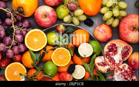 Fruits assortis. Différents fruits sur fond gris, toute la surface est couverte d'agrumes, de grenades, de pommes, de raisins, de fraises. Vue de dessus Banque D'Images