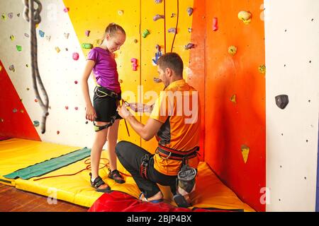 Entraîneur aider la petite fille à mettre sur l'équipement dans la salle de gym d'escalade Banque D'Images