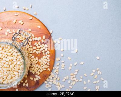 Bocal en verre avec des noix de cèdre de Sibérie debout sur un stand en bois sur un fond gris. Écrous dispersés sur la surface. Aliments végétaux organiques riches en vitamine Banque D'Images