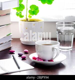 Une tasse de café blanche avec des bonbons multicolores se tient sur une table en bois, à côté d'une pile de livres et un carnet contre Banque D'Images