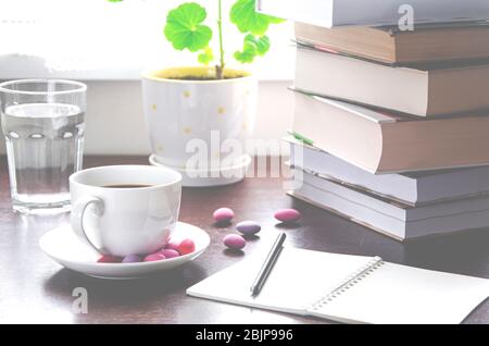 Une tasse de café blanche avec des bonbons multicolores se tient sur une table en bois, à côté d'une pile de livres et un carnet contre Banque D'Images