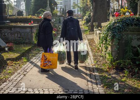 Un couple promenades remplies de sacs en plastique avec des fleurs sur le cimetière de Rakowicki à Cracovie, Pologne 2019. Banque D'Images