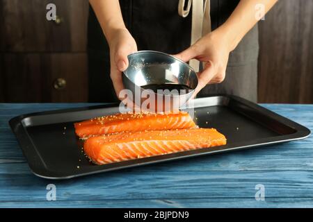 Femme préparant le filet de saumon avec la marinade de soja sur la plaque de cuisson Banque D'Images