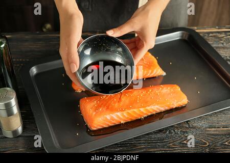 Femme préparant le filet de saumon avec la marinade de soja sur la plaque de cuisson Banque D'Images