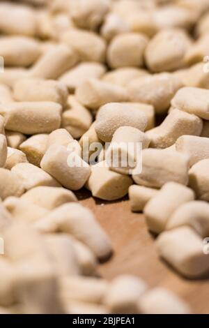 Boulettes italiennes gnocchi fraîches maison non cuites sur une planche en bois farinée dans une cuisine au basilic frais derrière dans une vue rapprochée Banque D'Images