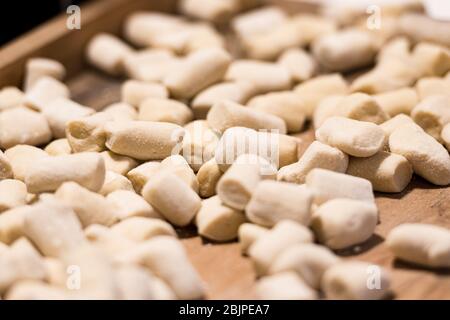 Boulettes italiennes gnocchi fraîches maison non cuites sur une planche en bois farinée dans une cuisine au basilic frais derrière dans une vue rapprochée Banque D'Images