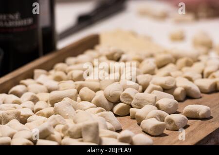 Boulettes italiennes gnocchi fraîches maison non cuites sur une planche en bois farinée dans une cuisine au basilic frais derrière dans une vue rapprochée Banque D'Images