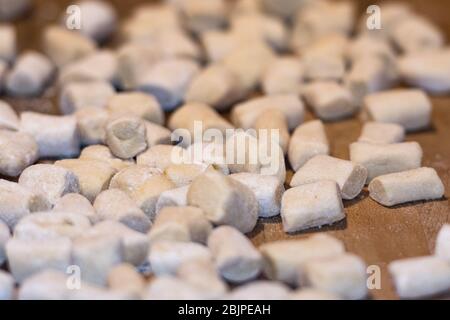 Boulettes italiennes gnocchi fraîches maison non cuites sur une planche en bois farinée dans une cuisine au basilic frais derrière dans une vue rapprochée Banque D'Images