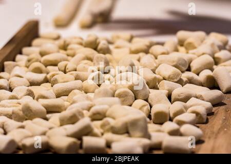 Boulettes italiennes gnocchi fraîches maison non cuites sur une planche en bois farinée dans une cuisine au basilic frais derrière dans une vue rapprochée Banque D'Images