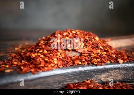 Flocons de piment rouge chaud dans une cuillère en bois se rapprochent sur une table de cuisine. Banque D'Images