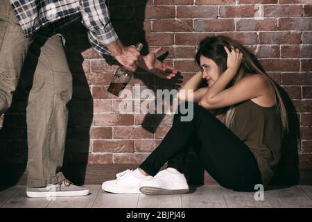 Homme avec bouteille d'alcool abuser la jeune femme contre le mur de brique Banque D'Images