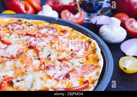 Pizza italienne au vrai pepperoni chaude sur la table avec des ingrédients. Délicieuse pizza maison fraîche avec salami, fromage, champignons, tomates, poivre. Italie Banque D'Images