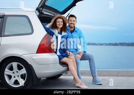 Jeune couple assis dans le coffre de voiture près de la rivière Banque D'Images
