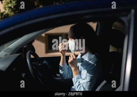 Femme caucasienne assise dans une voiture portant le masque de covid19 du coronavirus Banque D'Images