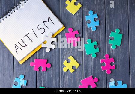 Mot AUTISME écrit dans le carnet et les puzzles sur fond de bois Banque D'Images
