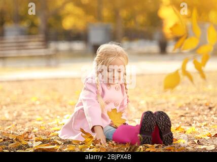 Cute little girl sitting on ground in autumn park Banque D'Images