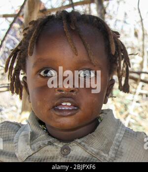 Jeune enfant de Maasai à l'entrée d'une hutte. Maasai est un groupe ethnique de personnes semi-nomades photographiées au Kenya Banque D'Images