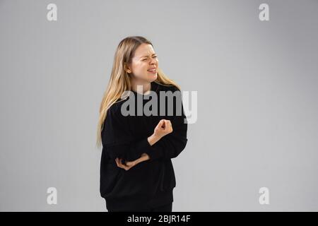 La jeune femme caucasienne souffre de douleurs coudées, se sent malade, malade et faiblesse isolérée sur fond gris de studio. Symptômes de malaise ou de style de vie malsain. Maladie, illidité, triste et bouleversée. CopySpace. Banque D'Images