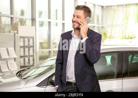 Bon vendeur de voiture parlant au téléphone dans le centre de la concession Banque D'Images