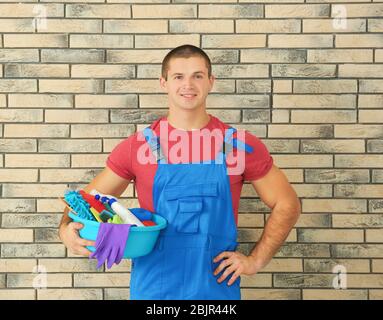 Jeune homme avec des fournitures de nettoyage sur fond de mur de briques Banque D'Images