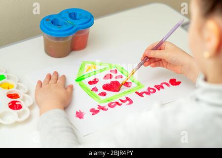 L'enfant dessine coeur à l'intérieur de la maison sur une feuille blanche de papier avec les mots rester à la maison. Concept de séjour à la maison. Banque D'Images