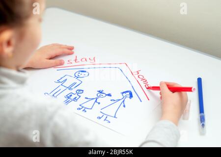 L'enfant écrit des mots rester à la maison avec la famille heureuse dessinée sur la feuille blanche de papier à la maison. Banque D'Images